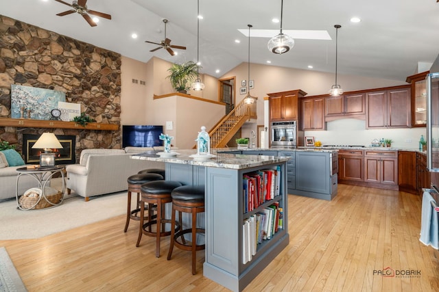 kitchen featuring appliances with stainless steel finishes, a fireplace, decorative light fixtures, a center island, and light stone counters