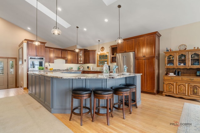 kitchen with hanging light fixtures, stainless steel appliances, a large island with sink, and light stone countertops