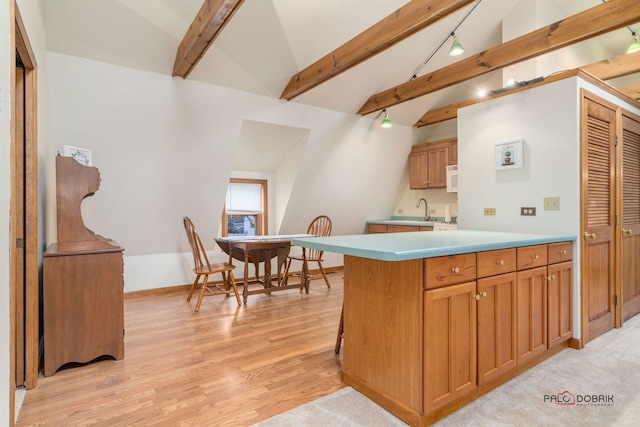 kitchen featuring a kitchen bar, kitchen peninsula, light hardwood / wood-style floors, and vaulted ceiling with beams