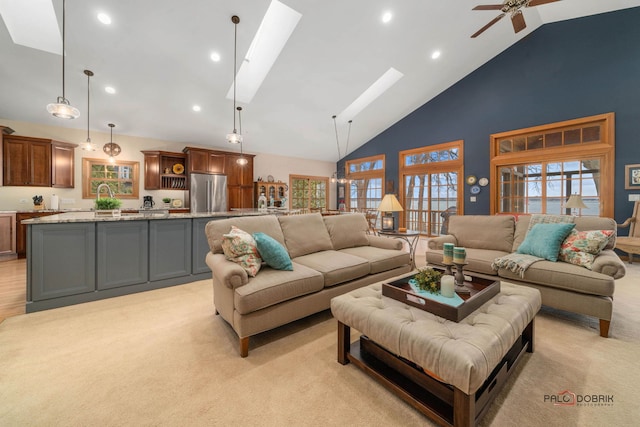 living room with high vaulted ceiling, a skylight, sink, ceiling fan, and light carpet