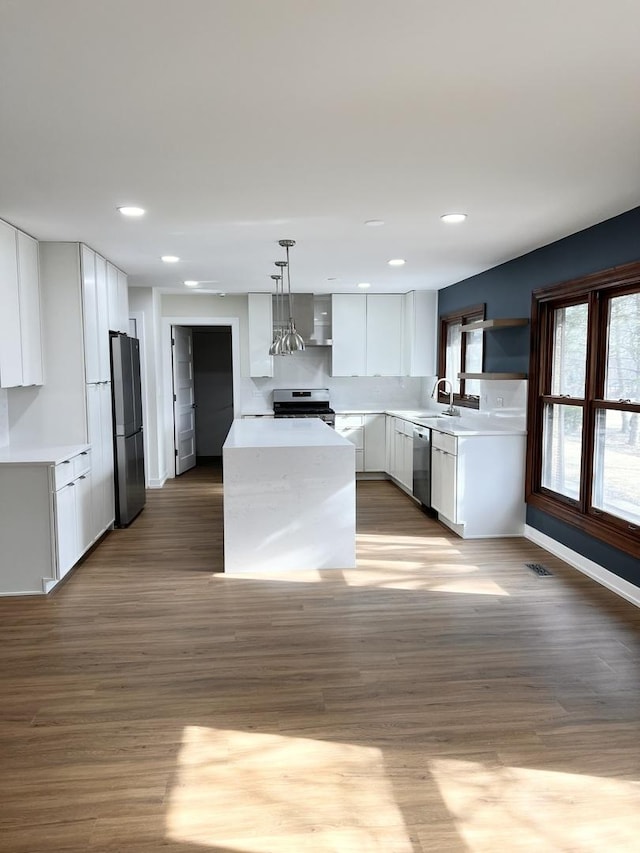 kitchen with white cabinetry, decorative light fixtures, stainless steel appliances, light hardwood / wood-style floors, and wall chimney range hood