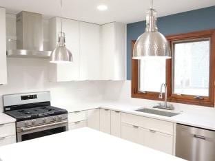 kitchen with pendant lighting, wall chimney range hood, sink, appliances with stainless steel finishes, and white cabinets