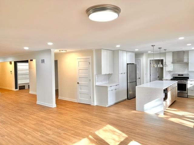 kitchen with wall chimney exhaust hood, white cabinetry, a center island, appliances with stainless steel finishes, and pendant lighting