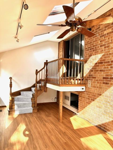 unfurnished living room featuring hardwood / wood-style flooring, rail lighting, ceiling fan, and brick wall