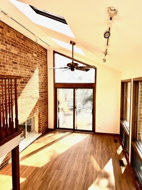 interior space with hardwood / wood-style flooring, vaulted ceiling, brick wall, and rail lighting