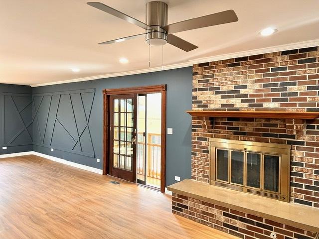 unfurnished living room with ceiling fan, ornamental molding, a fireplace, and light wood-type flooring