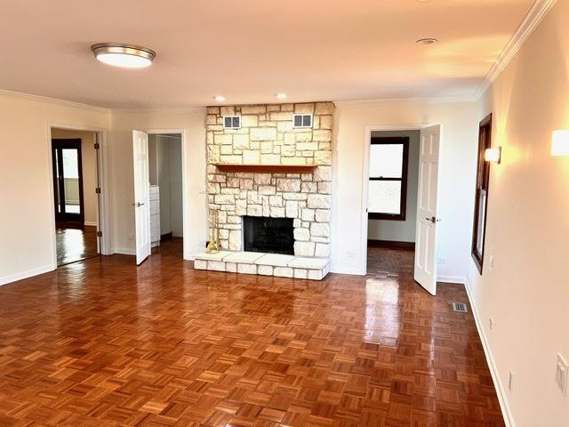 unfurnished living room with ornamental molding, a stone fireplace, and dark parquet floors