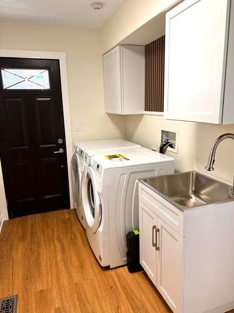 laundry area with light hardwood / wood-style floors, cabinets, separate washer and dryer, and sink