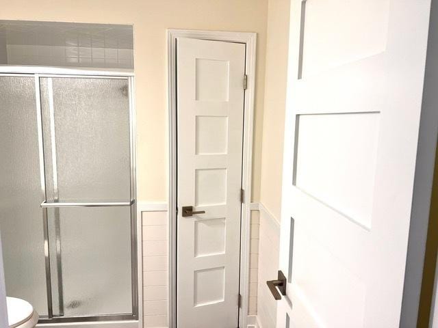 bathroom featuring tile walls, a shower with door, and toilet