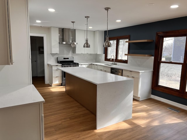 kitchen featuring decorative light fixtures, a center island, wall chimney range hood, stainless steel appliances, and white cabinets