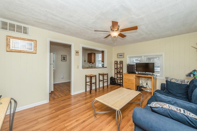 living room with a textured ceiling, ceiling fan, and light wood-type flooring