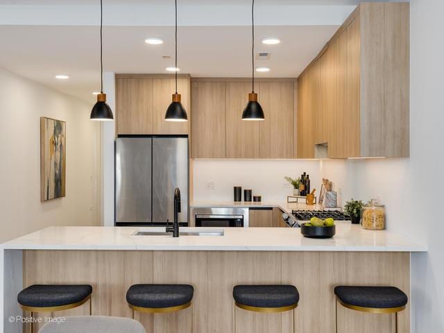 kitchen featuring a breakfast bar, light brown cabinetry, stainless steel refrigerator, sink, and kitchen peninsula