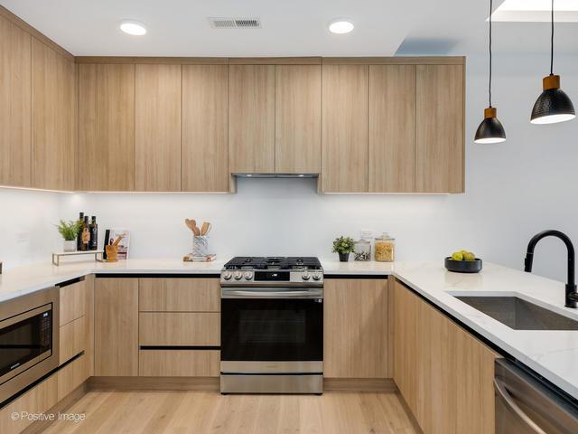 kitchen with light brown cabinetry, sink, decorative light fixtures, stainless steel appliances, and light stone countertops