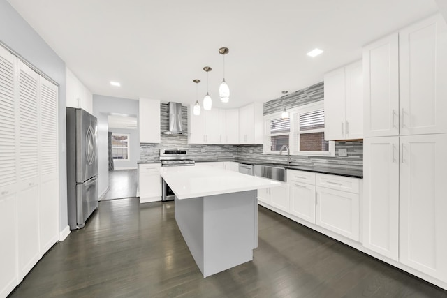 kitchen with wall chimney exhaust hood, stainless steel appliances, decorative light fixtures, and white cabinets