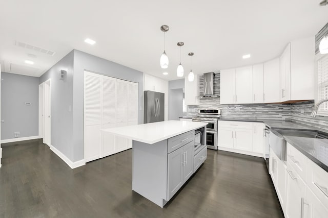 kitchen with white cabinetry, decorative light fixtures, a center island, stainless steel appliances, and wall chimney range hood