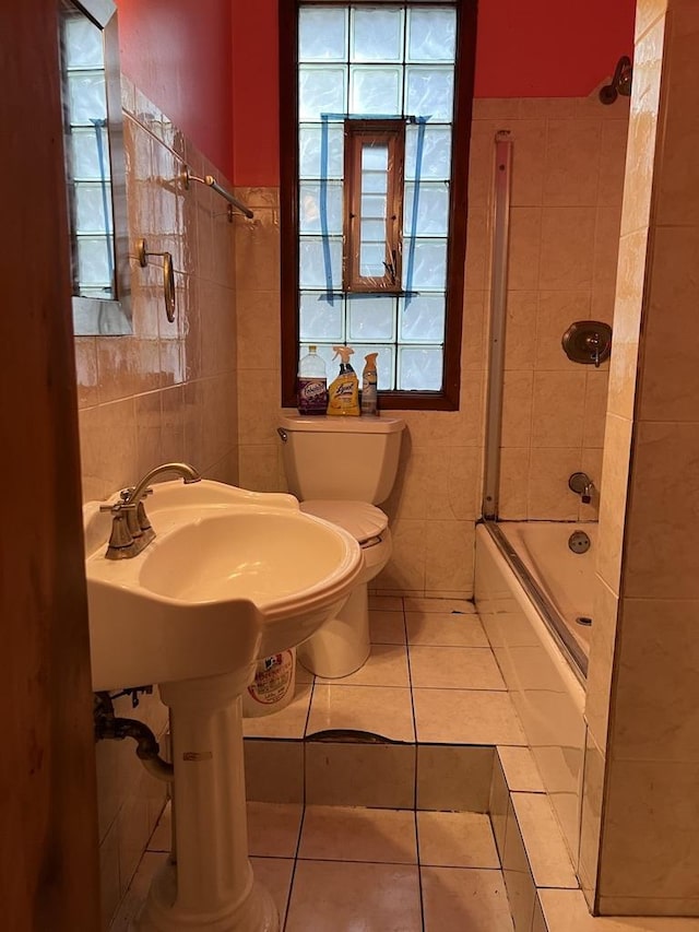 bathroom featuring tile patterned flooring, bath / shower combo with glass door, tile walls, and toilet