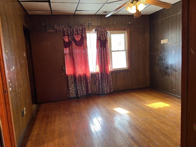 spare room featuring hardwood / wood-style flooring, ceiling fan, wooden walls, and a drop ceiling