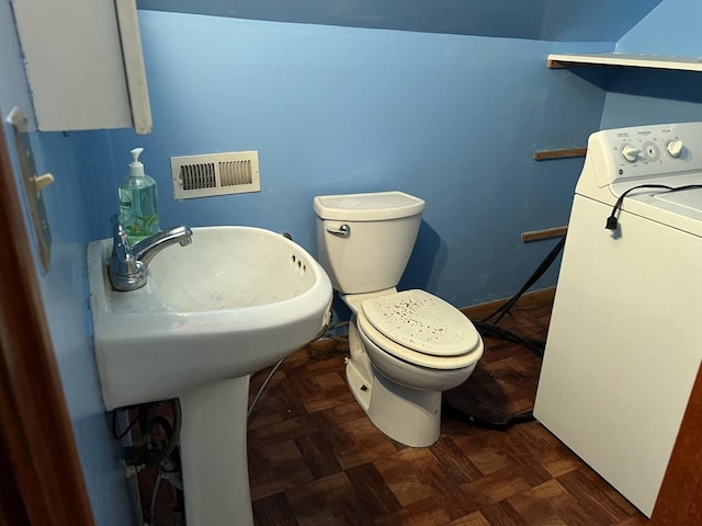 bathroom with parquet flooring, toilet, and washer / dryer