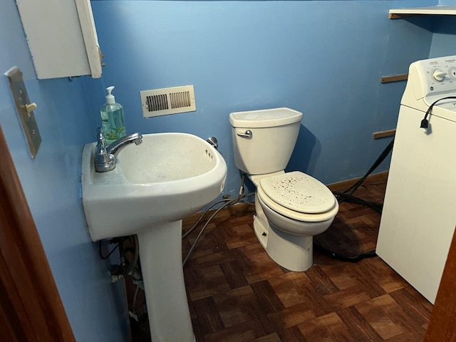 bathroom featuring parquet floors, toilet, and washer / dryer