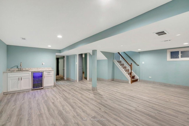 basement with beverage cooler, light wood-type flooring, and wet bar