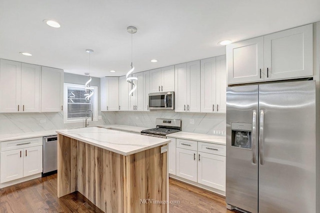 kitchen featuring pendant lighting, white cabinetry, hardwood / wood-style floors, stainless steel appliances, and tasteful backsplash