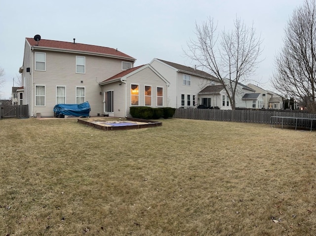 rear view of property featuring a trampoline and a lawn