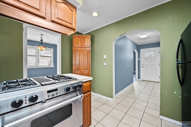 kitchen with arched walkways, light tile patterned floors, light countertops, freestanding refrigerator, and high end range