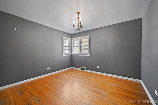 empty room featuring wood-type flooring, visible vents, a notable chandelier, and baseboards