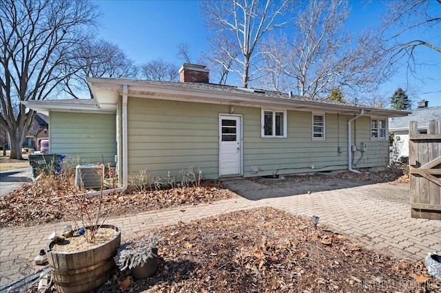 rear view of property with central air condition unit, a chimney, and a patio