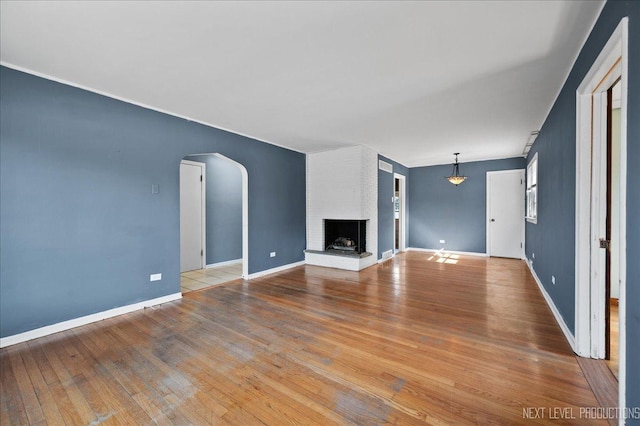 unfurnished living room with hardwood / wood-style flooring, baseboards, a brick fireplace, and arched walkways