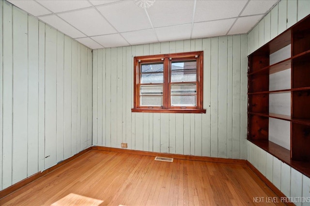 empty room featuring baseboards, visible vents, a drop ceiling, and light wood finished floors