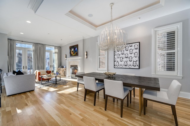 dining space with a raised ceiling, ornamental molding, light hardwood / wood-style floors, and french doors