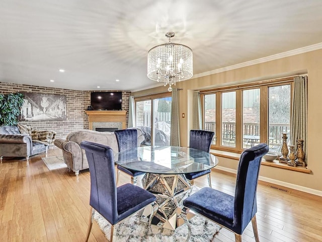 dining area with ornamental molding, brick wall, an inviting chandelier, and light wood-type flooring