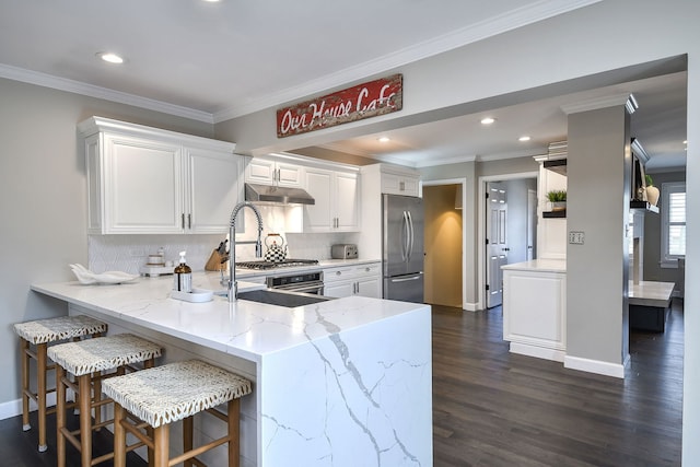 kitchen featuring under cabinet range hood, a peninsula, built in refrigerator, white cabinetry, and light stone countertops