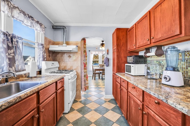 kitchen with crown molding, under cabinet range hood, arched walkways, white appliances, and a sink