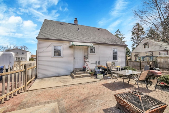 rear view of property with a fire pit, a shingled roof, fence, a chimney, and a patio