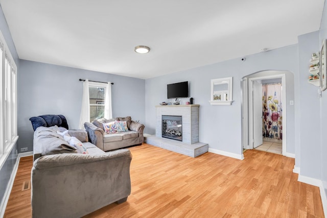 living area featuring baseboards, arched walkways, a fireplace, and light wood finished floors