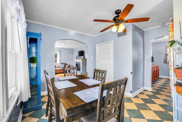 dining room featuring light floors, visible vents, a fireplace with raised hearth, arched walkways, and ornamental molding