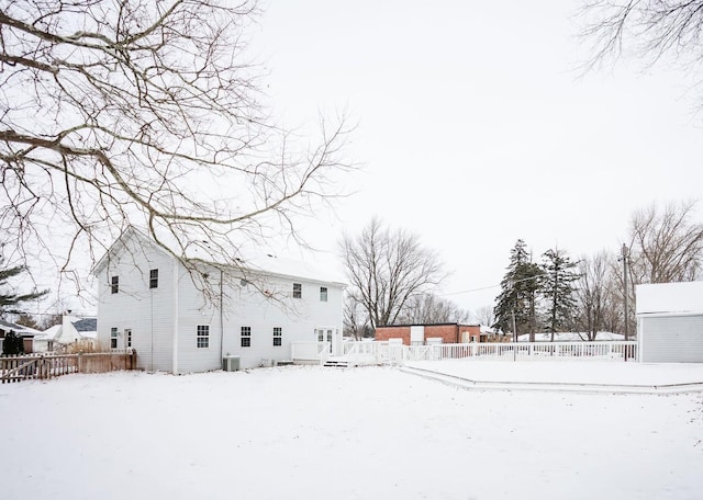 snow covered house featuring central AC unit, an outdoor structure, fence, and a wooden deck