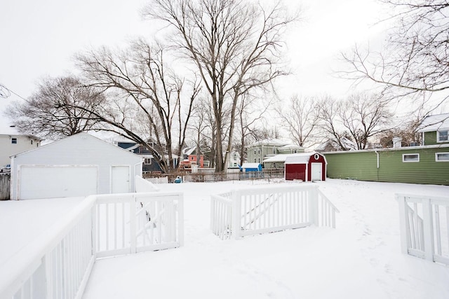 yard layered in snow featuring a garage, a storage unit, fence, and an outbuilding