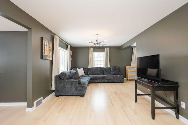 living room featuring an inviting chandelier, light wood-style flooring, visible vents, and baseboards