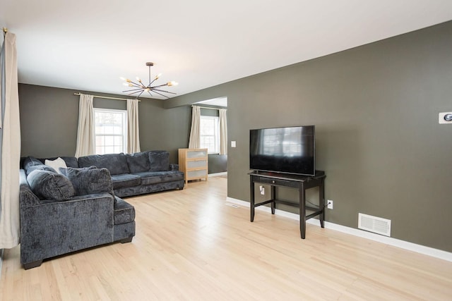 living room featuring a chandelier, baseboards, visible vents, and light wood finished floors