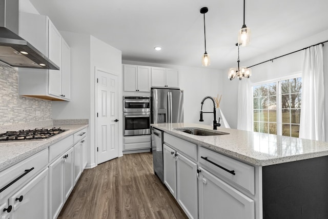 kitchen with wall chimney range hood, sink, a kitchen island with sink, light stone counters, and white cabinets