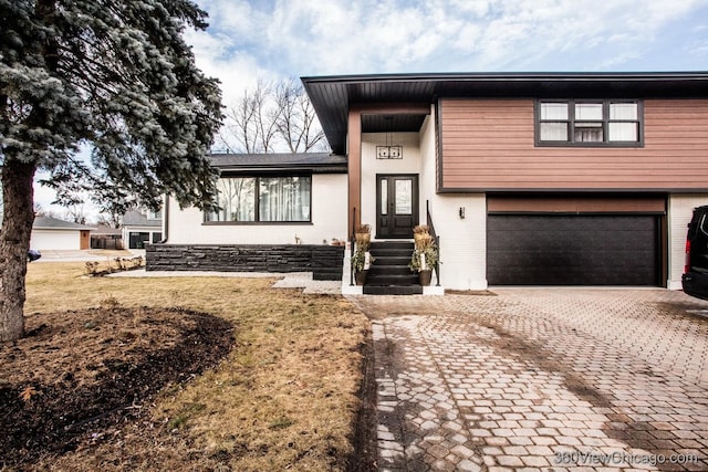 split level home featuring a front yard, decorative driveway, brick siding, and an attached garage