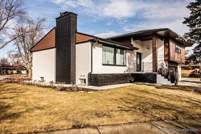 view of property exterior featuring a garage, brick siding, a chimney, and a lawn