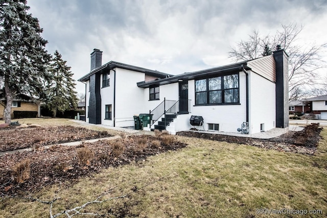 split level home featuring entry steps, a chimney, a front lawn, and brick siding