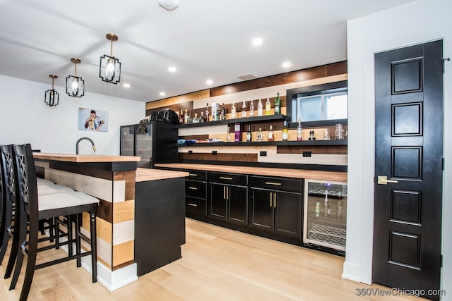 bar with light wood finished floors, wine cooler, wet bar, and decorative light fixtures