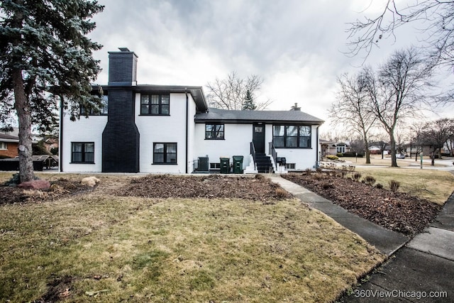 view of front of property featuring entry steps, a front lawn, a chimney, and central air condition unit