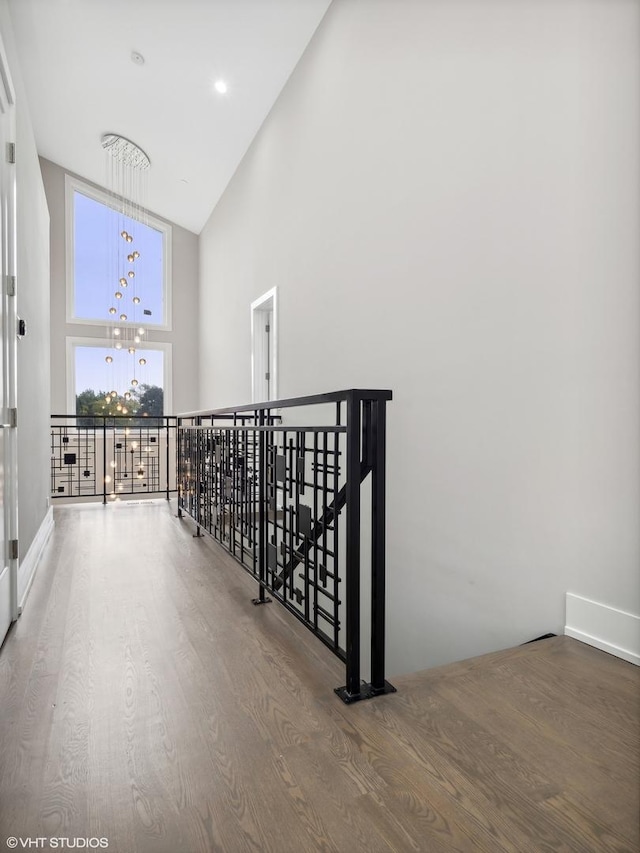 hallway with high vaulted ceiling, hardwood / wood-style floors, and an inviting chandelier