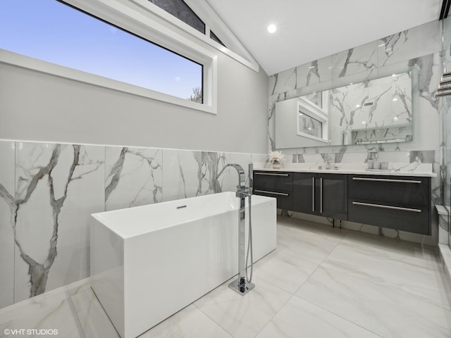 bathroom featuring vanity, vaulted ceiling, tile walls, and a tub